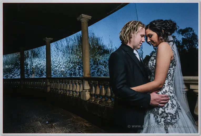 Andrew and Jenna lean foreheads together by a lit waterfall wall at Caversham House in blue dusk light.