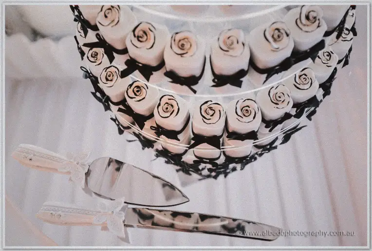 Close-up of the tiered cake with white chocolate roses tied in black ribbon and a lace-handled knife.
