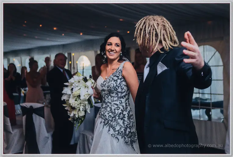 Jenna beams with a white lily bouquet as Andrew greets cheering guests inside the draped marquee.