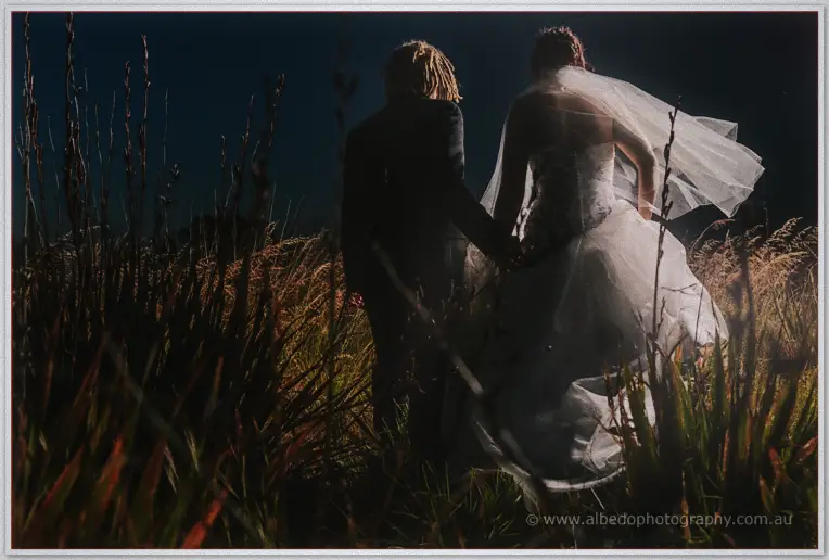 Andrew leads Jenna hand in hand through tall golden grass, her veil catching the last light after sunset.