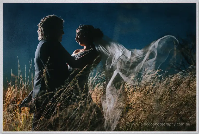 Jenna's veil billows as Andrew holds her in windswept grass against the night sky.