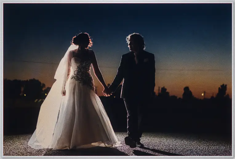 Silhouetted hand in hand at nightfall, Jenna's gown flowing as they walk the estate grounds.