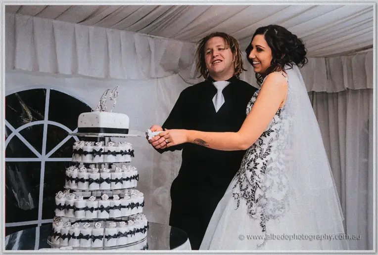 Jenna and Andrew laugh while cutting their white and black wedding cake together in the marquee.