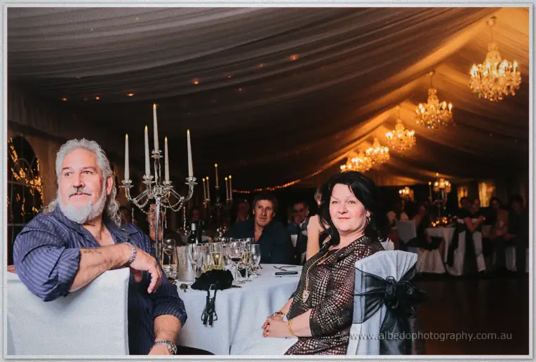 Guests relax around candle-lit tables beneath glowing chandeliers in the warmly lit reception marquee.