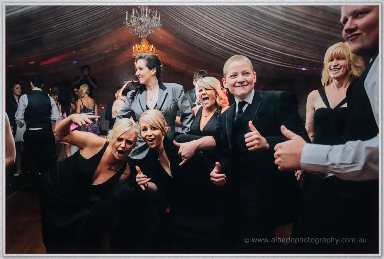 Guests in black give thumbs up and clown for the camera on the packed dance floor.