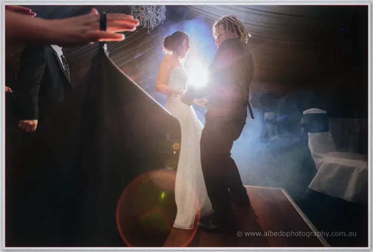 Jenna and Andrew dance through haze and lens flare as guests raise their hands around the floor.