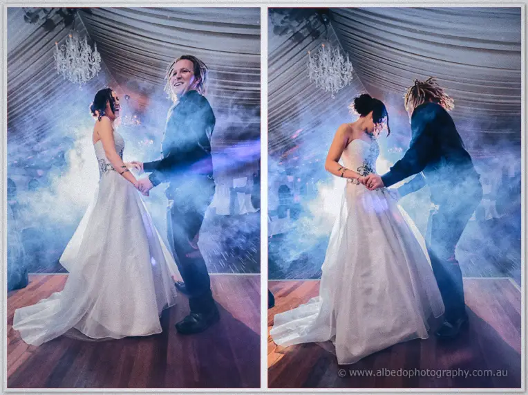 Jenna and Andrew hold hands mid-dance in swirling blue smoke under the marquee chandelier, both laughing.