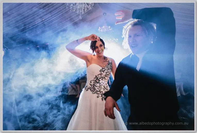Jenna raises an arm mid-spin beside Andrew on the smoke-filled dance floor, lit by bright party lights.
