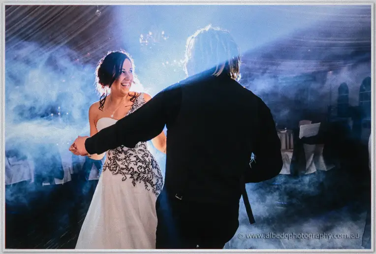 Andrew reaches back for Jenna's hand as they dance, her white gown glowing in the blue haze.