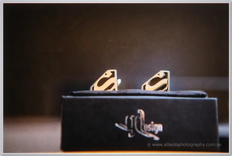 Superman shield cufflinks gleam atop a black presentation box in moody morning light