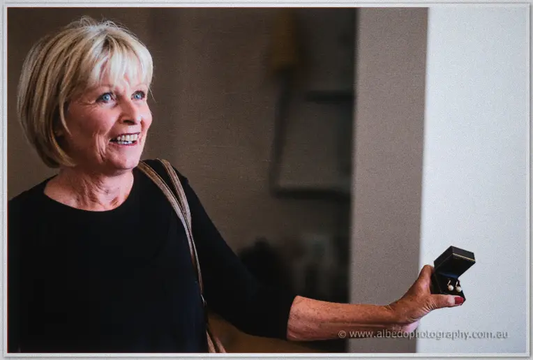 A smiling blonde mother holds out the ring box in the hotel's softly lit hallway