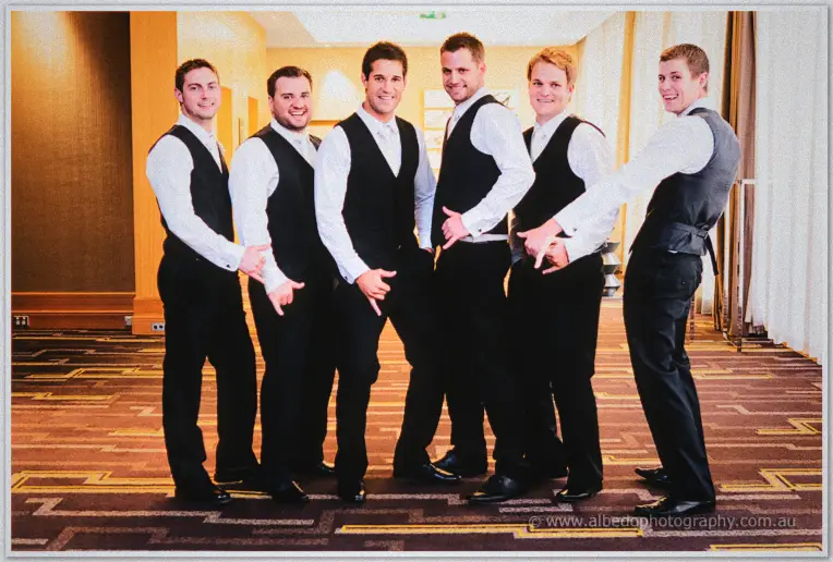 Nathan and his groomsmen strike playful hand-sign poses in the hotel corridor