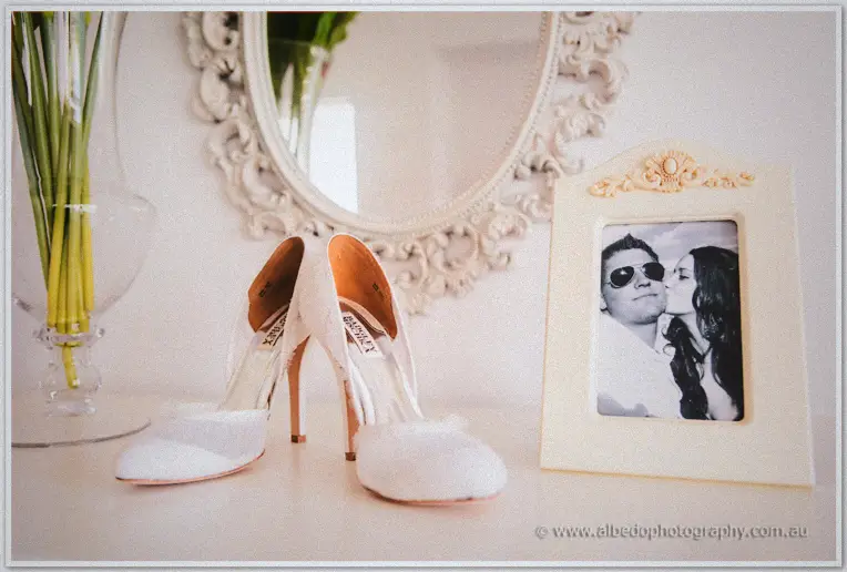 Lace bridal heels and a framed couple's portrait sit before an ornate white mirror