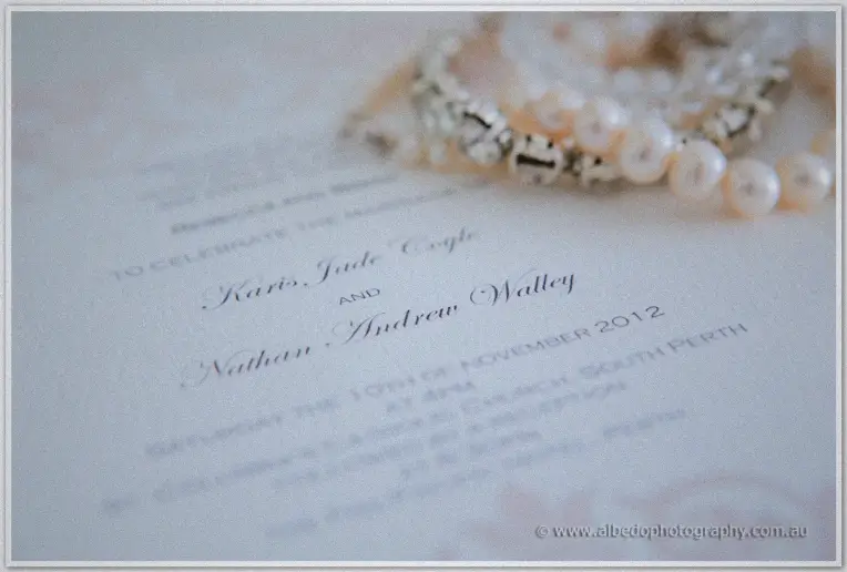 Karis and Nathan's invitation rests beneath pearl jewellery in soft pastel light