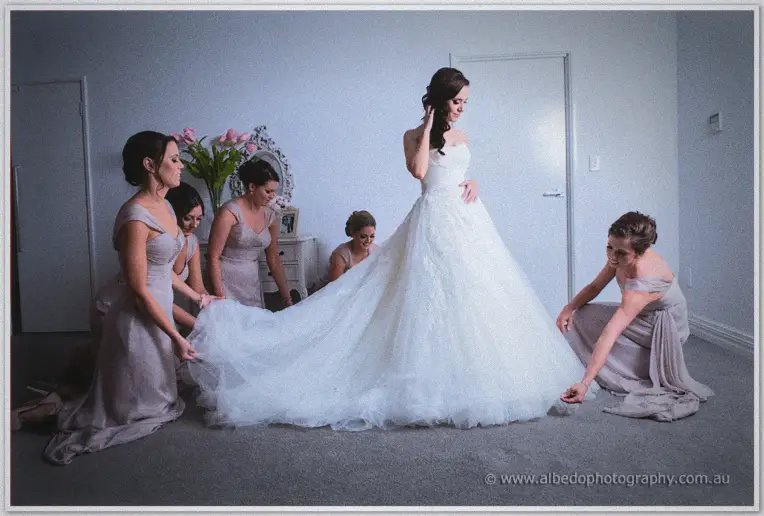 Bridesmaids kneel to arrange the full tulle train of Karis's strapless wedding gown