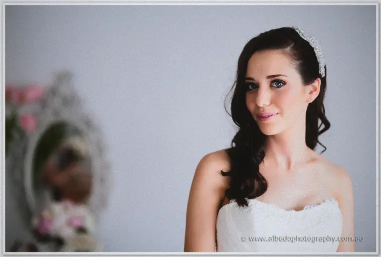 Karis wears a crystal headpiece and strapless lace gown, turning in soft window light