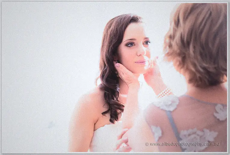 An older woman gently cups the bride's face in bright airy morning light