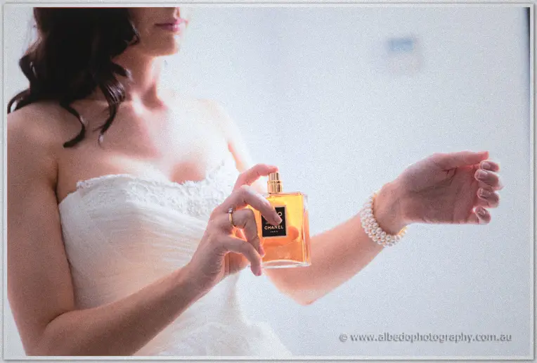 Close view of Karis dabbing amber perfume on her wrist above a pearl bracelet