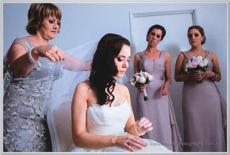 Karis is seated while her veil is arranged and bridesmaids wait with peony bouquets