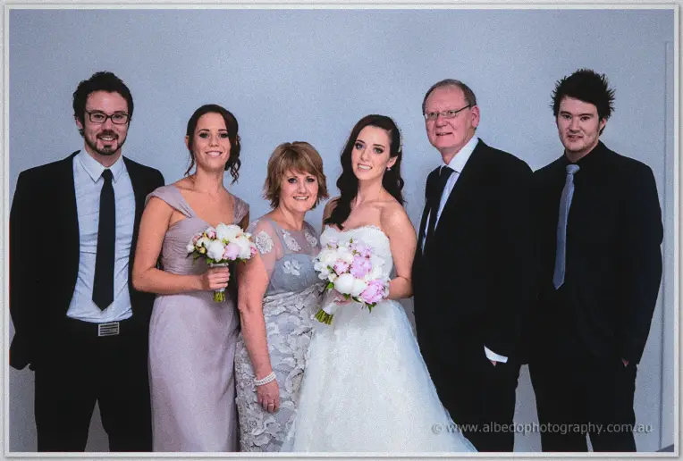 Karis poses with her parents and two brothers in suits before a plain white wall