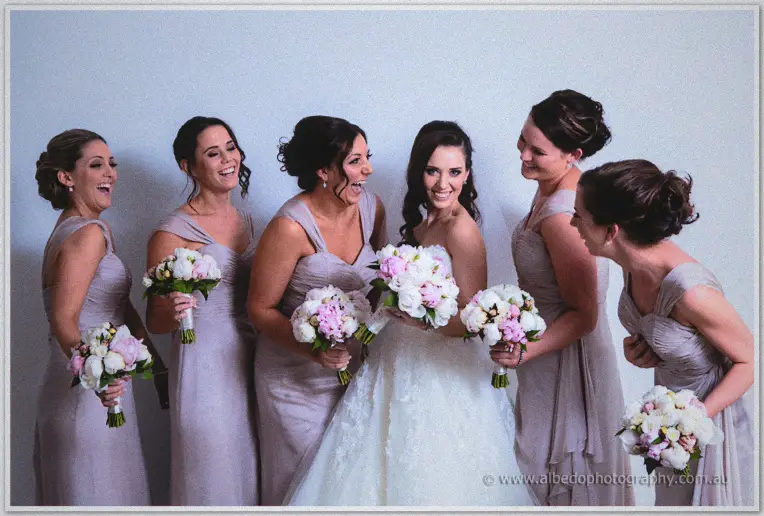 The bridal party bursts out laughing around Karis as she lifts her bouquet