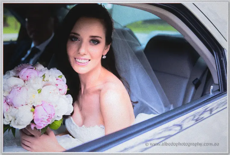 Karis beams from the car seat cradling her pink and white peony bouquet