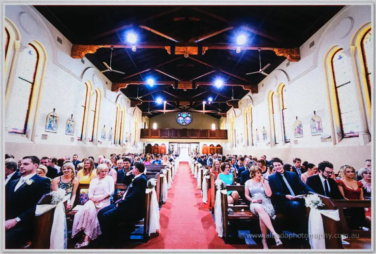 Guests fill wooden pews along a red aisle inside a warm timber-beamed church