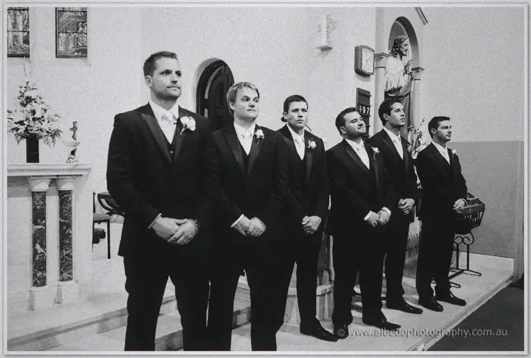 Nathan and his groomsmen stand tense at the altar in a black and white wide shot