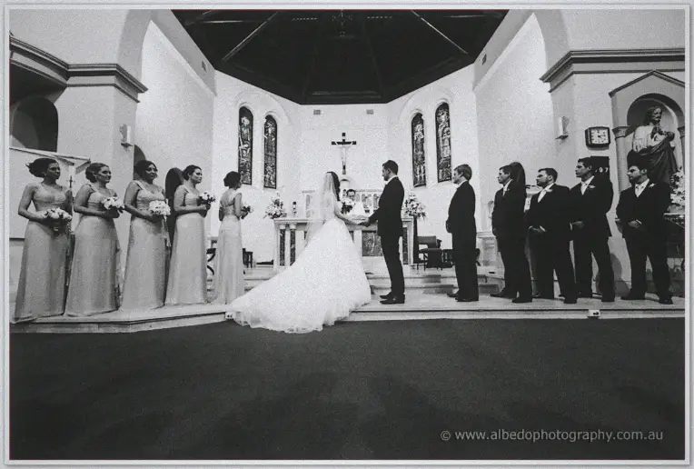 Wedding party lined at the altar during vows in a black and white churchwide view