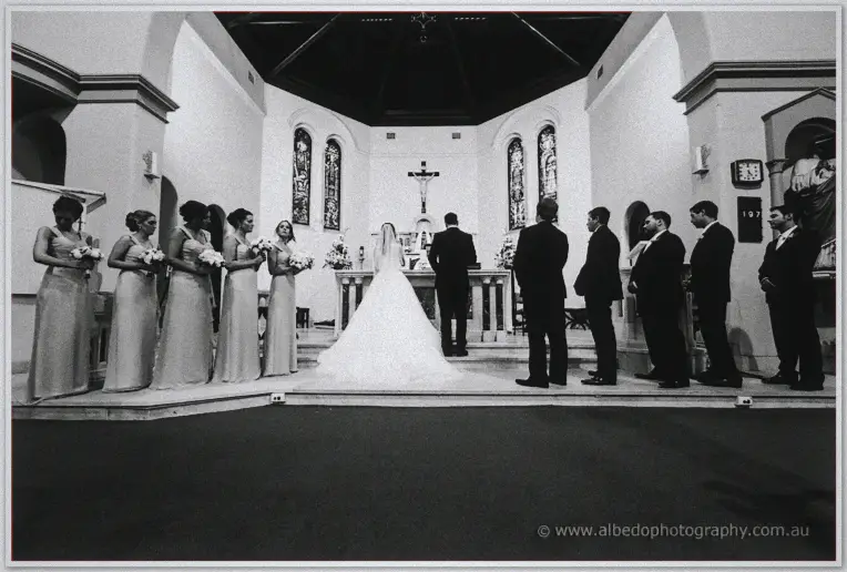 Karis and Nathan face the altar before bridesmaids and groomsmen in a black and white wide
