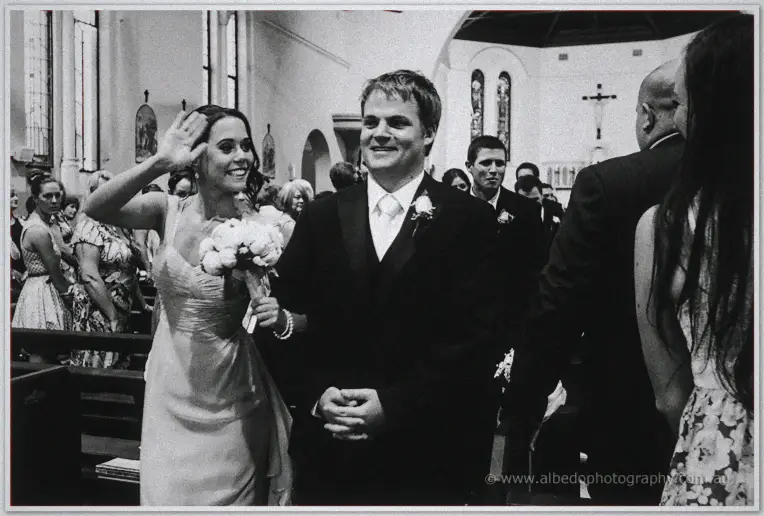 Karis waves to standing guests as she and Nathan walk back up the aisle