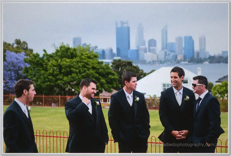 Nathan and his groomsmen laugh on a lawn beneath the Perth skyline and river