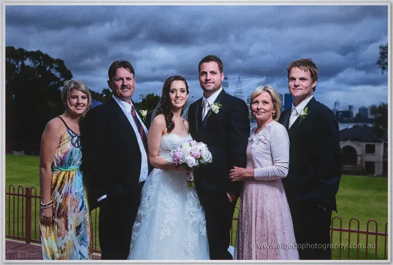 Karis and Nathan stand with family beneath storm clouds on the lawn above the Swan River in Perth