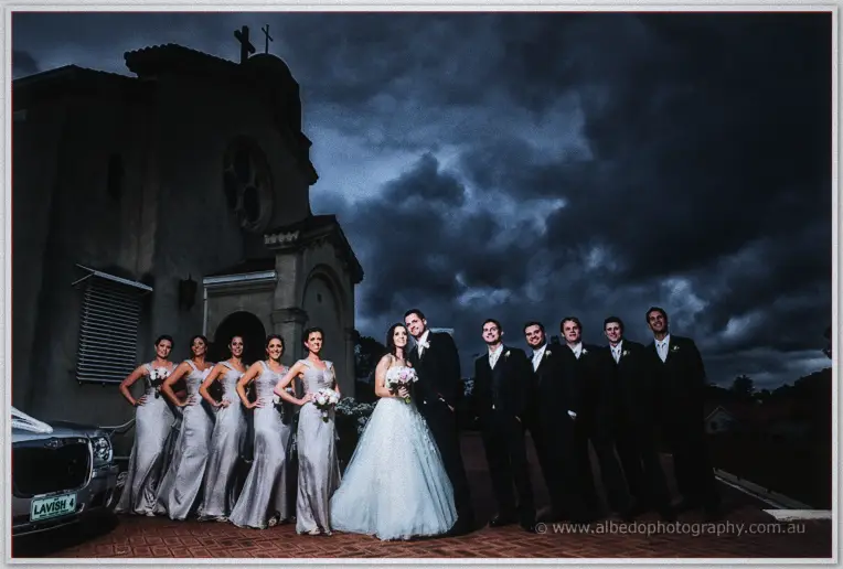 Karis and Nathan line up with bridesmaids in grey and groomsmen in suits outside the stormy church
