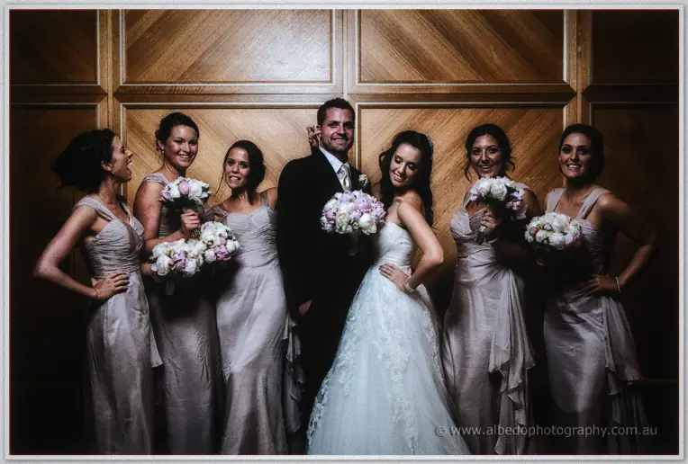 Nathan joins Karis and the bridesmaids for a playful group portrait in front of the hotel's timber panelling
