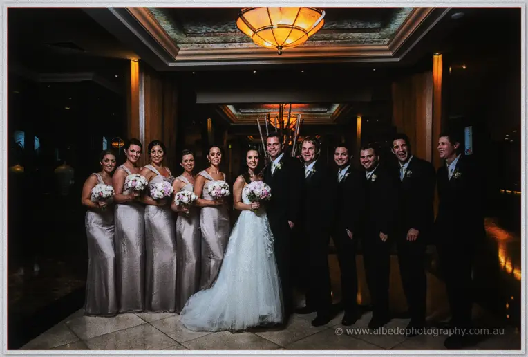 The whole bridal party gathers in the hotel lobby, lit warm by a chandelier overhead
