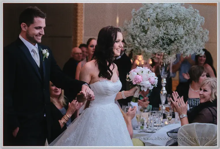 Karis and Nathan enter the ballroom hand in hand past clapping guests and baby's breath centrepieces