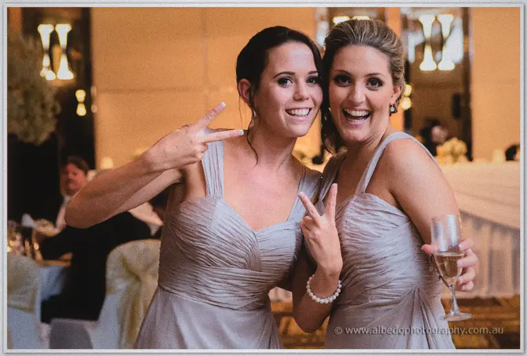 Two bridesmaids flash peace signs and champagne as they pose among the reception tables