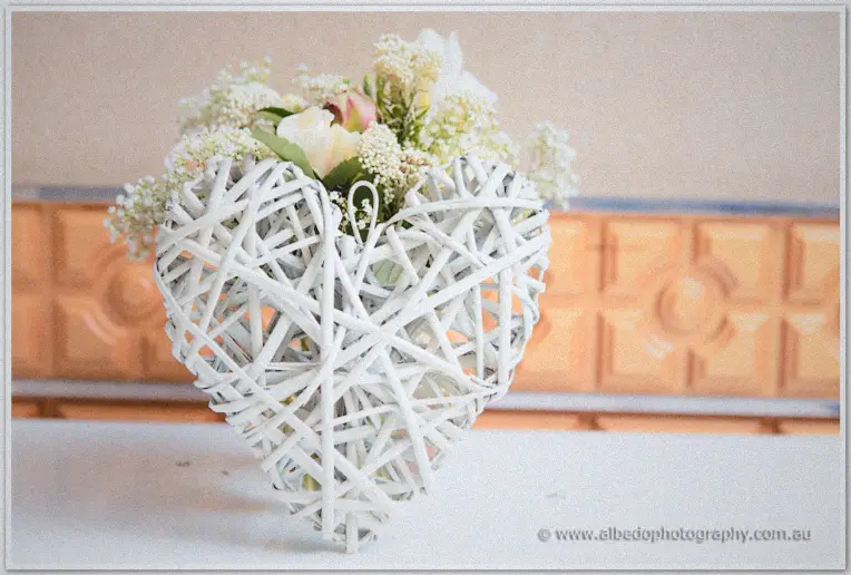 A white woven heart filled with baby's breath and roses sits on the signing table