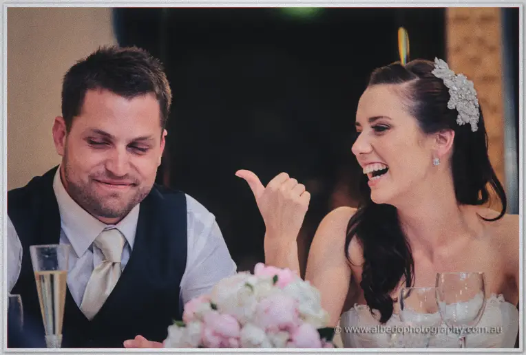 Karis cackles and points at Nathan over pink peonies during the speeches
