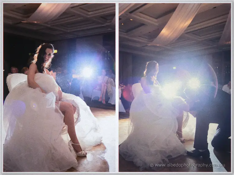 Karis sits laughing as Nathan lifts her leg for the garter retrieval on the dance floor