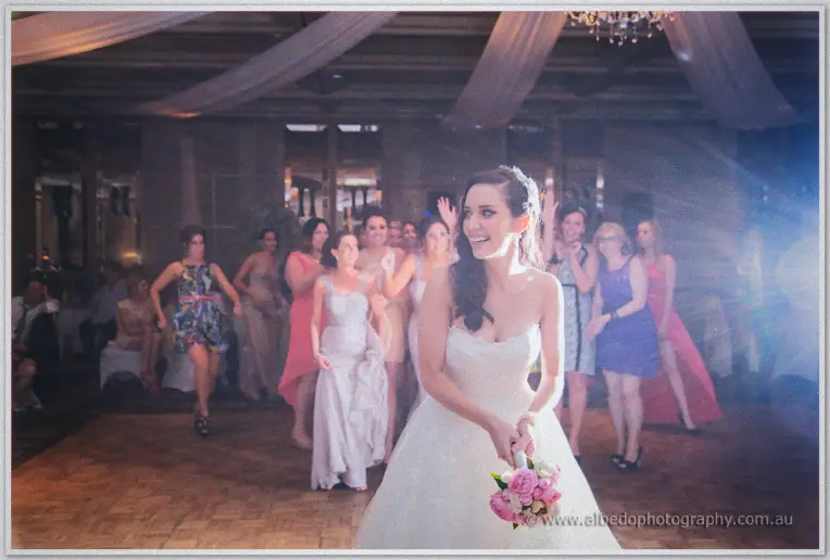 Karis turns to toss her pink bouquet to a crowd of lunging bridesmaids