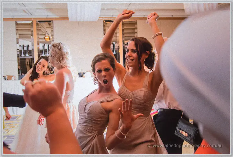 Two bridesmaids dance with arms flung high, one pulling a fierce face for the camera