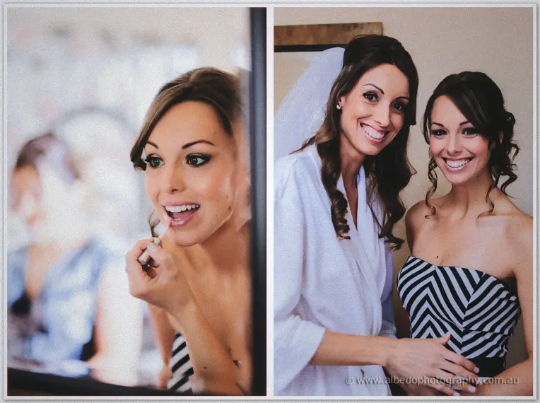 Bride applying lip gloss in a mirror and laughing with a bridesmaid in a striped strapless dress