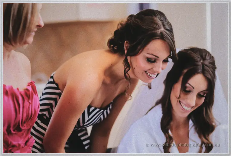Bridesmaids in pink and black-striped dresses leaning in laughing beside the smiling bride in her robe