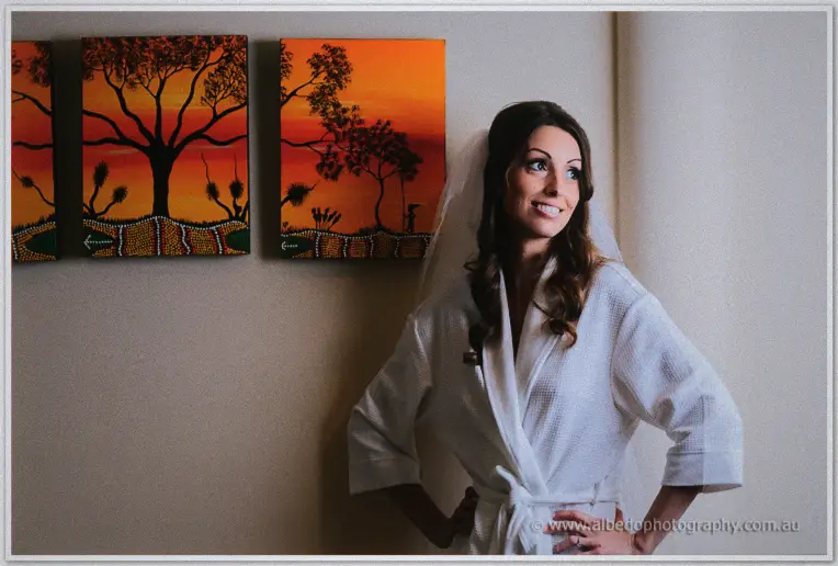 Smiling bride in a white robe and veil posing beneath vivid orange outback paintings