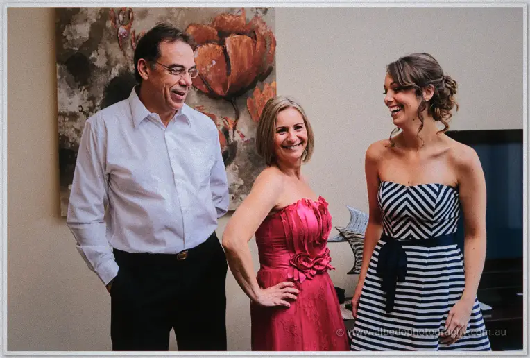 Parents of the bride laughing together in a lounge, mother in a pink ruffled dress, father in white shirt