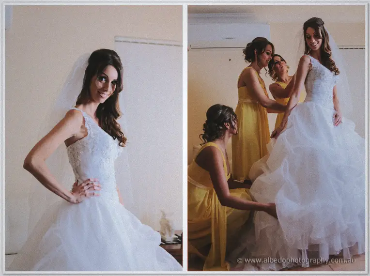 Bride in a one-shoulder lace gown as yellow-dressed bridesmaids arrange her full ruffled skirt