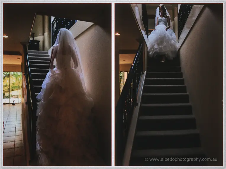 Bride descending a dim staircase from behind, her long veil glowing in the light above
