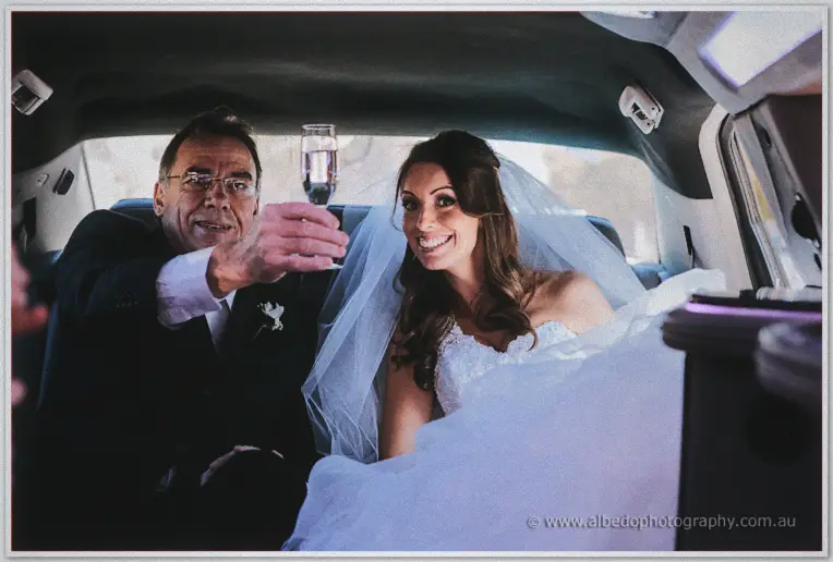 Bride and her father raising a champagne toast inside a dimly lit stretch limousine